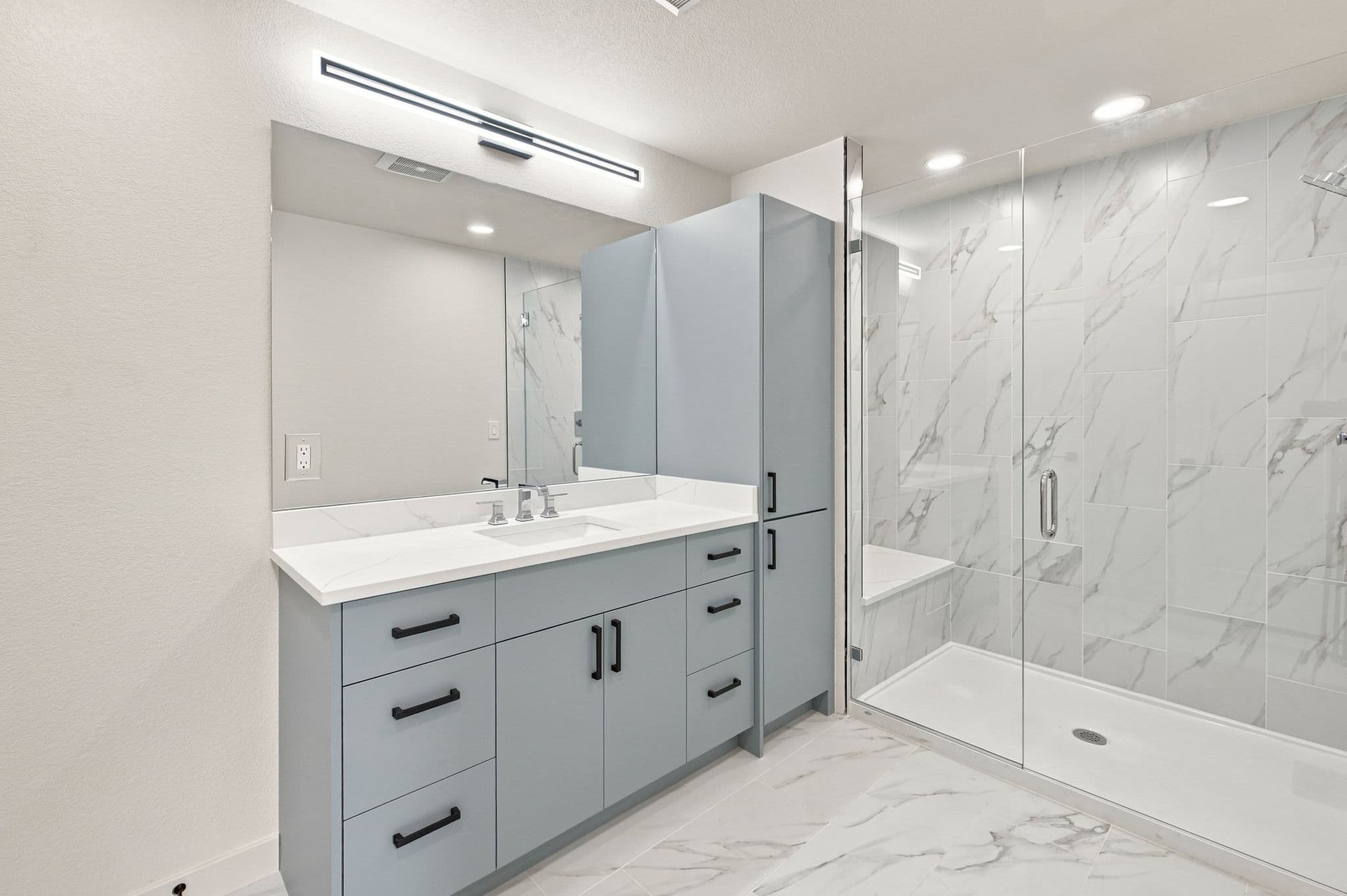 Full bath with quartz vanity, linen cabinet, LED lighting, and frameless glass shower